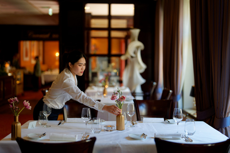 Servicemitarbeiterin dekoriert einen eingedeckten Restauranttisch – Reportagefoto für ein Hotelmagazin